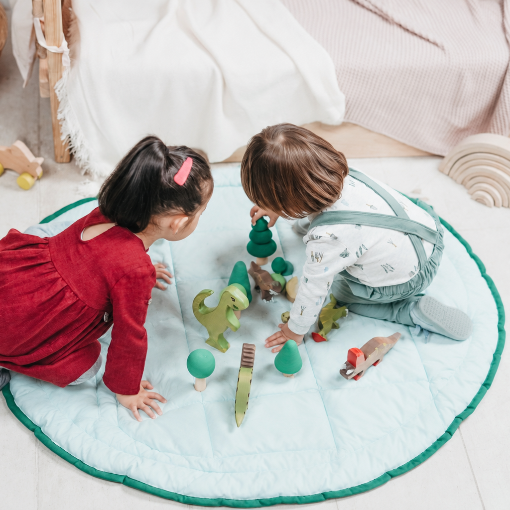 Two children playing with toys on a green and white spacious organic play mat in a cozy room.